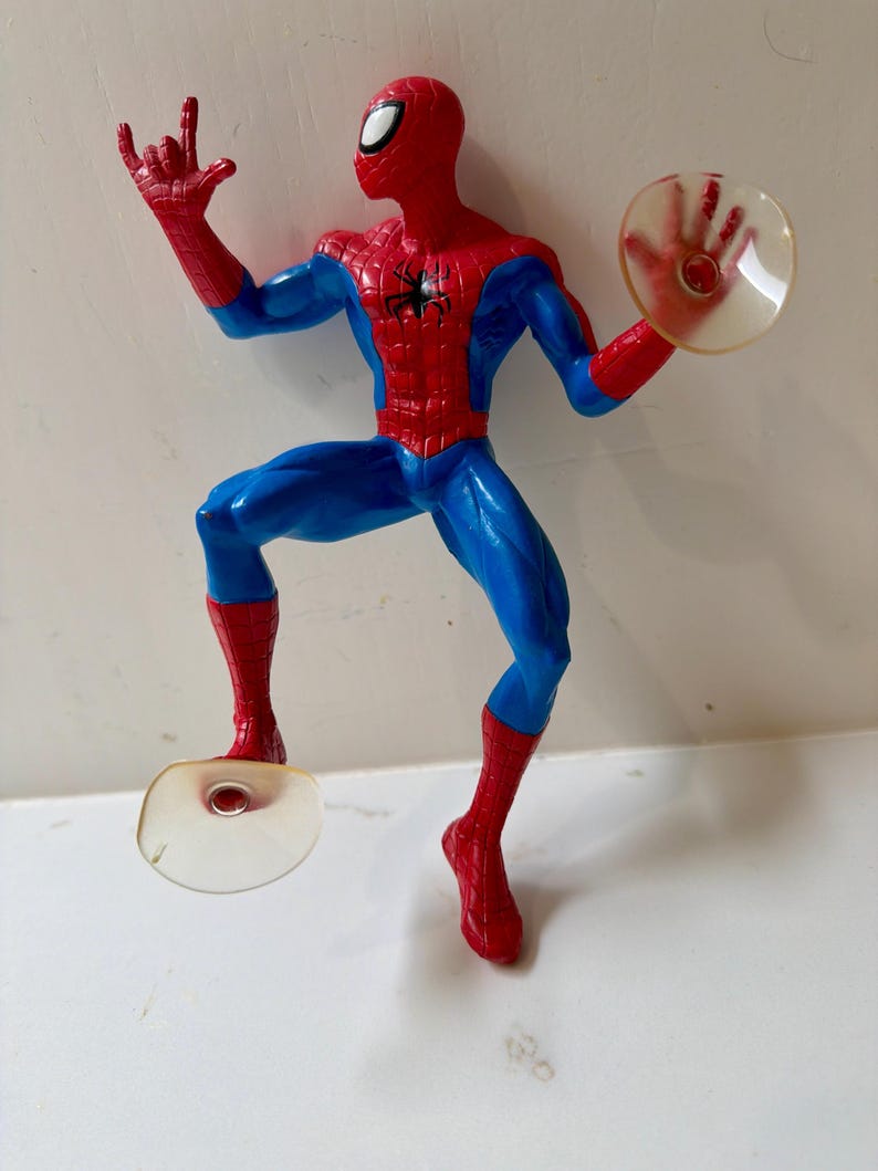 May include: A Spider-Man action figure in a dynamic pose, featuring a red and blue costume. The figure has a red mask with white eye lenses, a black spider emblem on the chest, and is holding a clear disc in one hand. The figure is approximately 6 inches tall.