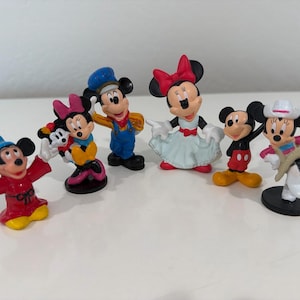 May include: A collection of seven small Mickey and Minnie Mouse figurines. The figurines feature Mickey and Minnie in various outfits, including a cowboy, a conductor, and a sorcerer. The figurines are brightly colored and made of plastic.