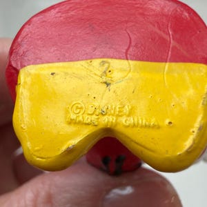 May include: Close-up of a red and yellow figurine. The figurine's base is yellow with the text "&copy; Disney Made in China". The top is red. The figurine is a collectible item.