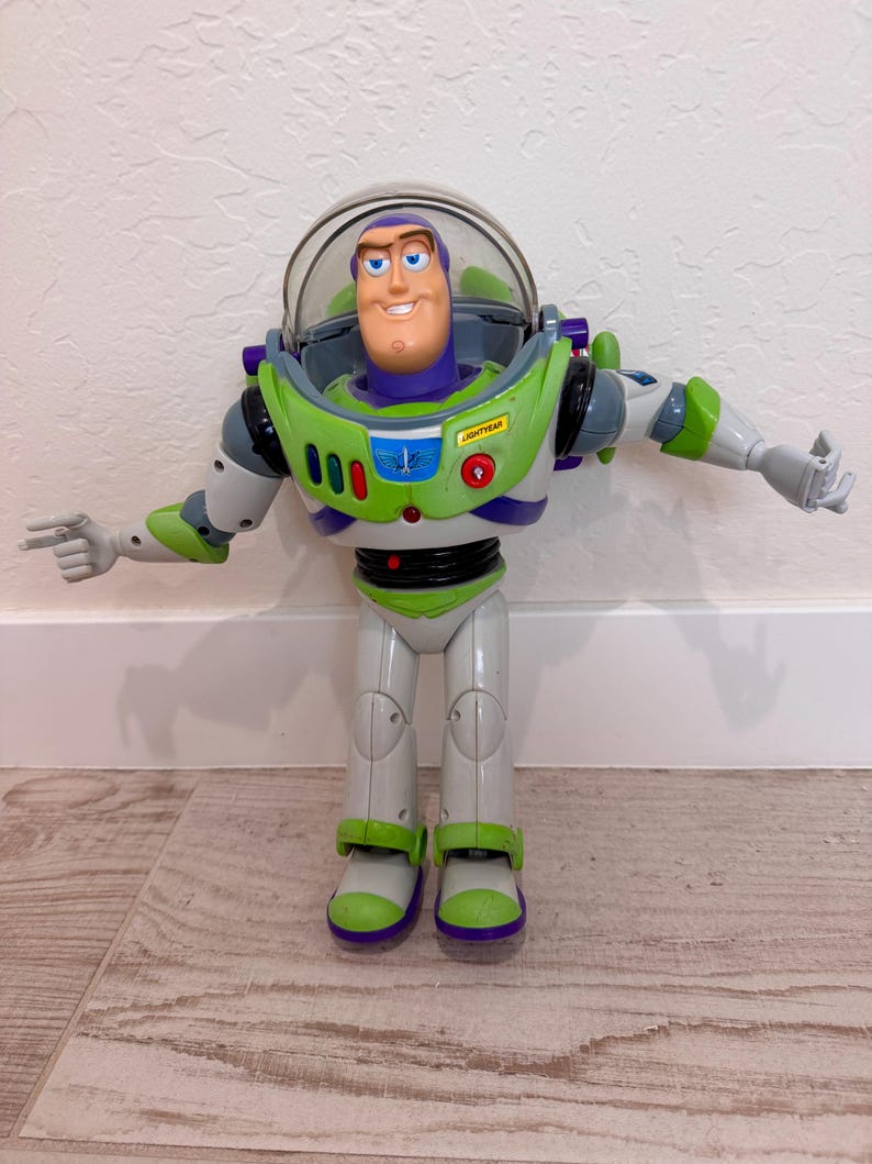 May include: A Buzz Lightyear action figure from the Toy Story franchise. The figure is primarily white, green, and purple, with a clear plastic helmet. The figure has its arms outstretched and is standing on a wooden floor.