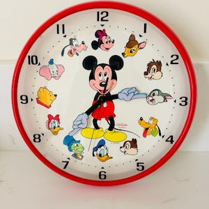 May include: A round wall clock with a bright red frame and a white face featuring black numbers and various Disney character illustrations. Mickey Mouse is in the center with arms acting as clock hands. The Sunbeam Quartz logo is printed on the face.