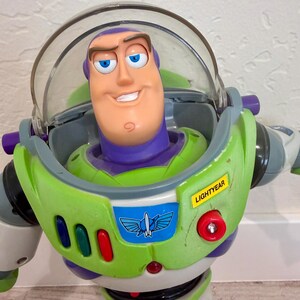 May include: A Buzz Lightyear action figure, featuring a green and white spacesuit with purple accents. The figure has a clear helmet, a smiling face, and the name "LIGHTYEAR" on the chest. The toy is a popular character from the Toy Story franchise.