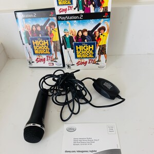 May include: A PlayStation 2 video game titled Disney High School Musical Sing It! with its game case, a tall promotional box, a black wired microphone with a control module, and a white registration card with Disney Interactive Studios address.