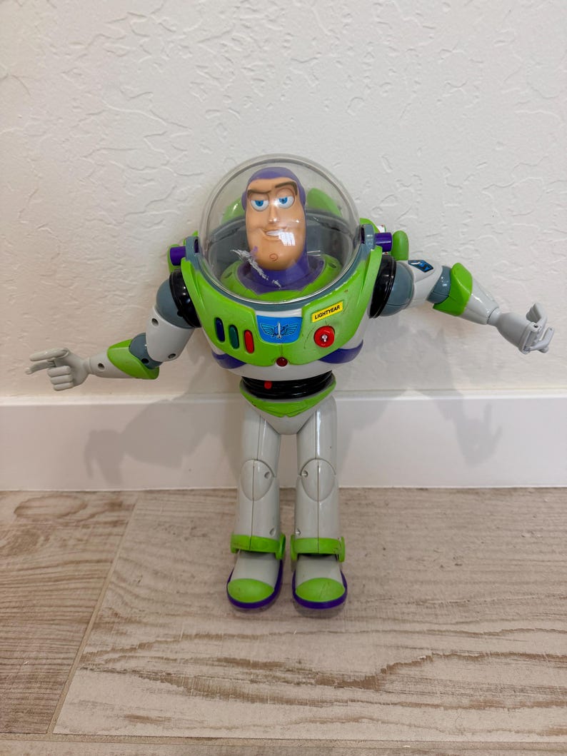 May include: A Buzz Lightyear action figure, featuring a green and white spacesuit with purple accents. The figure has a clear helmet, a smiling face, and outstretched arms. The word "LIGHTYEAR" is visible on the chest.
