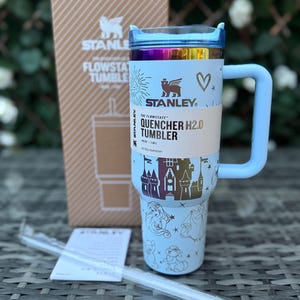 May include: A light blue Stanley Quencher H2.0 Tumbler with a handle, straw, and box. The tumbler features a castle and princess design, with the text "QUENCHER H2.0 TUMBLER". The tumbler holds 40 oz (1.18 L).