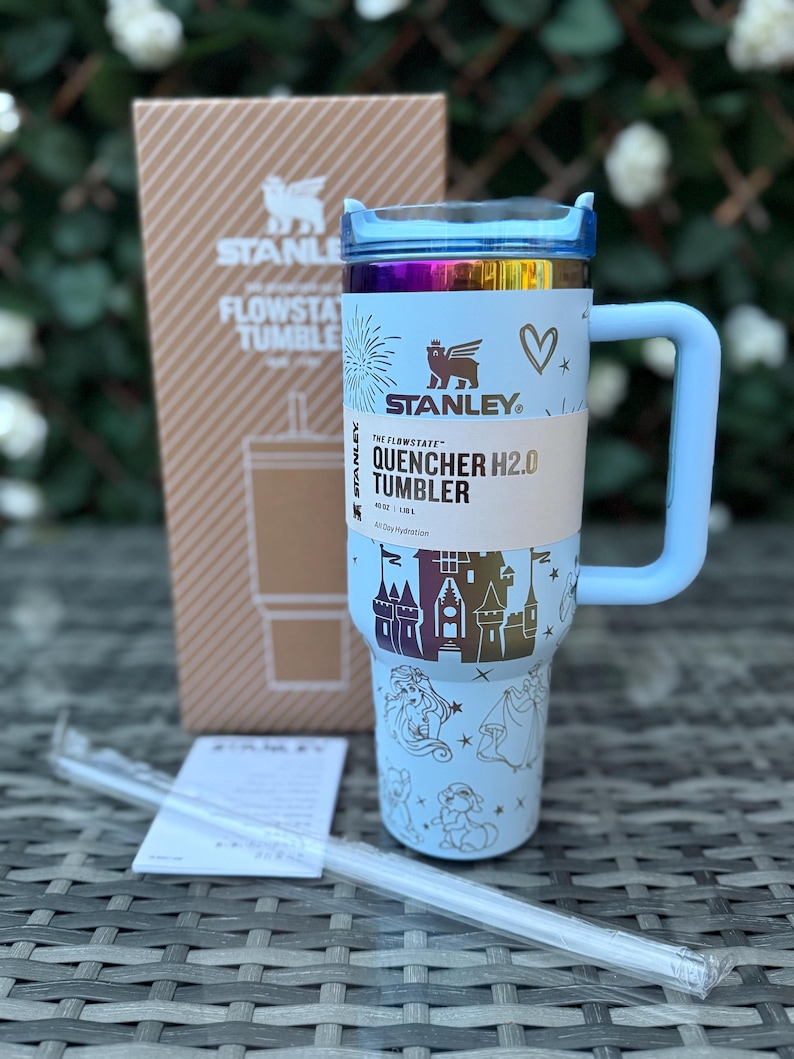 May include: A light blue Stanley Quencher H2.0 Tumbler with a handle, straw, and box. The tumbler features a castle and princess design, with the text "QUENCHER H2.0 TUMBLER". The tumbler holds 40 oz (1.18 L).