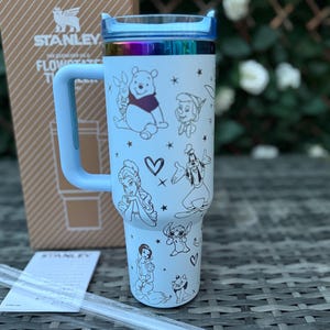 May include: A light blue Stanley Flowstate tumbler with a handle and a rainbow-colored lid. The tumbler features black line drawings of Disney characters, including Winnie the Pooh, and a clear straw.