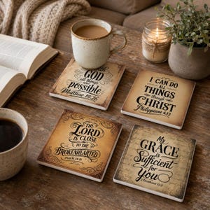 May include: Four square coasters with a vintage parchment-style background and black decorative borders. Each coaster features a unique Bible verse: Matthew 19:26, Philippians 4:13, Psalm 34:18, and 2 Corinthians 12:9, written in varied typography.