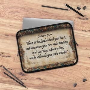 May include: A rectangular laptop sleeve featuring a parchment-style background with an ornate, colorful border. The text reads: Proverbs 3:5-6, Trust in the Lord with all your heart, and lean not on your own understanding; in all your ways submit to him, and he will make your paths straight.