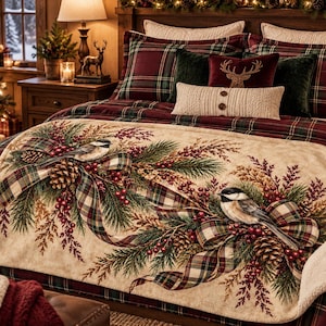 May include: A cream-colored throw blanket featuring a print of two chickadees perched on pine branches with pinecones, red berries, and a plaid ribbon. The blanket has a soft, textured underside and is draped over a bed with plaid bedding.