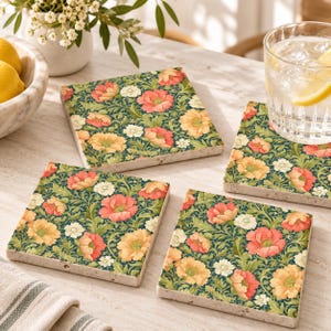 May include: A set of three square stone coasters featuring a dense botanical pattern of orange, red, and white flowers with green foliage on a dark background. The coasters have a smooth, flat surface and a light-colored, textured stone edge.
