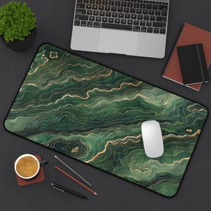May include: A rectangular desk mat featuring a dark green and gold marbled pattern with flowing, wavy lines. The surface has a smooth texture and a black border, providing a wide area for computer peripherals like a mouse and keyboard.
