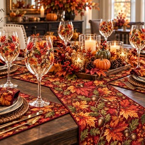 May include: A fall-themed table setting featuring wine glasses decorated with colorful autumn leaves, a matching table runner, placemats, and napkins. The centerpiece includes small pumpkins, pinecones, and candles in glass holders.