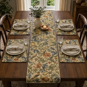 May include: A dining table set featuring a long rectangular table runner and four matching placemats, all decorated with a detailed floral and bird pattern in shades of green, blue, and orange. Four white plates with beige napkins are included.