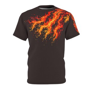 May include: A dark brown t-shirt with a fiery design in red, orange, and yellow. The flame pattern flows diagonally across the upper left of the shirt. The t-shirt has short sleeves and a crew neck, creating a dynamic visual effect.
