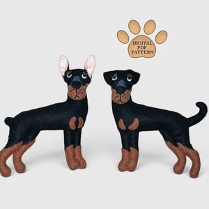 May include: Two felt dog plushies featuring black and tan fur, upright ears, and embroidered facial details. Above the dogs is a tan paw print graphic containing the text DIGITAL PDF PATTERN. The dogs are standing in a side profile position.