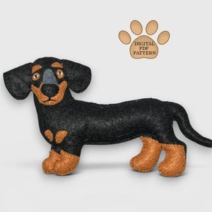 May include: A handmade felt dachshund dog toy in black and brown. The toy has large floppy ears, a long body, and short legs. The text "DIGITAL PDF PATTERN" is in a paw print graphic.