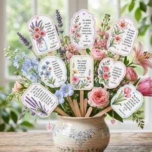 May include: A floral arrangement in a decorative vase, featuring a variety of pink, purple, and blue flowers. The bouquet includes several decorative wooden signs with floral designs and inspirational quotes. The vase has a blue and white pattern.