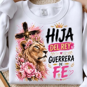 May include: A white crewneck sweatshirt featuring a graphic of a lion wearing a floral crown, positioned beneath a black cross. The text reads HIJA DEL REY GUERRERA DE FE, accompanied by a gold crown, pink brush strokes, small hearts, and a cross.