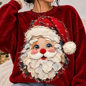 Puede incluir: Una sudadera de manga larga en color rojo intenso con una gran aplicación texturizada de Santa Claus. El diseño está hecho de piezas de tela superpuestas con bordes deshilachados, un gorro rojo con pompón blanco y un rostro detallado.