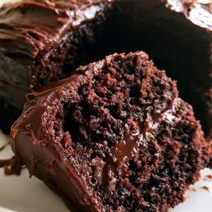 Op de afbeelding: Een stuk rijke chocoladetaart met donkere chocolade glazuur, op een wit bord. De taart heeft een vochtig, getextureerd uiterlijk, met een royale laag glanzend glazuur. Een klassiek dessert.