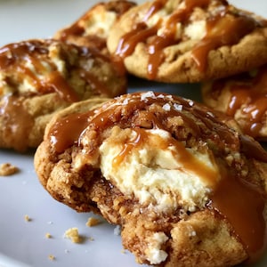 Könnte beinhalten: Nahaufnahme von mehreren Karamell-Cookies mit einer cremigen weißen Füllung, beträufelt mit Karamellsauce und bestreut mit grobem Salz. Die Kekse sind goldbraun und liegen auf einem weißen Teller.