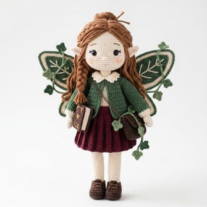 May include: A handcrafted crochet doll featuring brown hair in a braided style, pointed ears, and large black eyes. The doll wears a green cardigan, a white collared shirt, and a maroon pleated skirt. It has green wings with ivy accents.