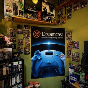May include: A room filled with retro video game consoles, games, and memorabilia. A large Dreamcast poster dominates the wall, with shelves holding PlayStation, Xbox, and Nintendo boxes. Plush Mario characters and a small TV add to the nostalgic atmosphere.