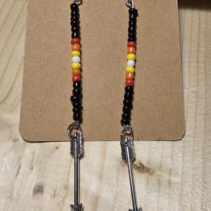 May include: A pair of long, beaded earrings with arrowhead charms. The beads are black, orange, yellow, and white.