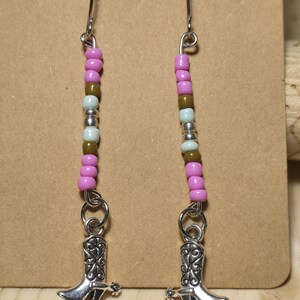 May include: A pair of silver dangle earrings with pink, brown, and silver beads and a silver cowboy boot charm.