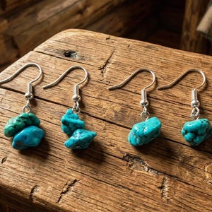 May include: Four individual dangle earrings featuring raw, irregular turquoise-colored stones suspended from silver-toned metal fishhook wires. Two earrings consist of stacked stone pieces, while the other two feature single stones.