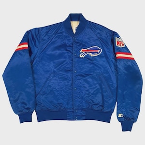 Puede incluir: Una chaqueta bomber de satén azul real con el logotipo de los Buffalo Bills en el pecho, un parche con el escudo de la NFL en la manga izquierda y el logotipo de Starter en el puño izquierdo. La chaqueta tiene rayas rojas y blancas en las mangas.