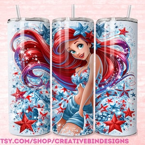 May include: A white tumbler featuring a patriotic design with a cartoon mermaid. The design includes red and blue stars, and the mermaid is wearing a star-spangled top and shorts. The tumbler has a silver lid and a straw.