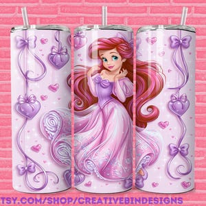 May include: A pink tumbler featuring a princess in a pink gown with long red hair. The tumbler is decorated with purple hearts, bows, and ribbons. The background is a light pink color with a brick pattern.