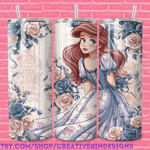 May include: A stainless steel tumbler featuring a princess illustration in a blue and white dress, surrounded by blue and pink roses. The tumbler has a straw and is decorated with a floral and architectural design. The text "PNG" is visible.
