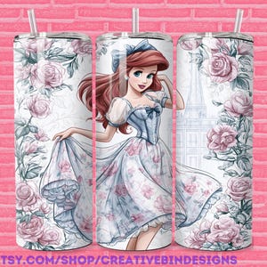 May include: A set of three stainless steel tumblers with a floral design and a cartoon illustration of a princess. The princess is wearing a blue dress and has red hair. The tumblers have a white background and are decorated with pink roses and green leaves. The tumblers have a straw.