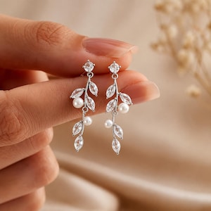 May include: A pair of silver-toned drop earrings featuring a delicate branch design. Each earring is adorned with multiple marquise-cut clear crystals and small round white pearls, suspended from a single round crystal stud at the top.