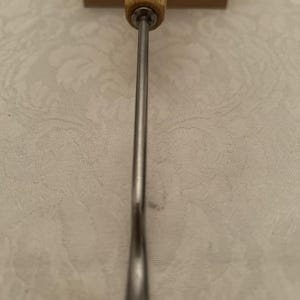 May include: A wood-handled carving tool with a long, slender, metal blade. The handle is light-colored wood, and the blade is silver. The word "SWISS" is visible on the handle. The tool is designed for detailed woodworking.