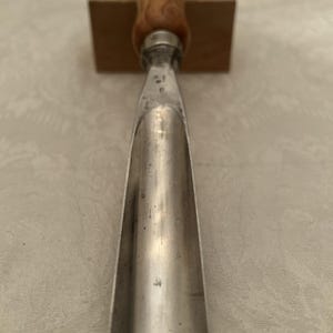 Puede incluir: Un formón de gubia de metal con mango de madera. El formón tiene una hoja curva y un mango de madera con un acabado marrón claro. La herramienta está diseñada para trabajar la madera y tallar.