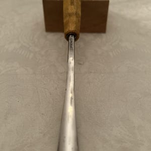 Könnte beinhalten: Ein Holzschnitzbeitel mit Holzgriff und silberner Klinge. Der Griff ist hellbraun und trägt den Aufdruck "SWISS MADE". Die Klinge ist silberfarben und verjüngt sich zu einer Spitze.