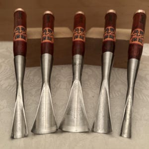 May include: Five wood carving gouges with polished metal blades and dark wooden handles. Each handle features a copper-colored metal cap at the top and a rectangular orange label with black Japanese text wrapped around the upper portion of the wood.