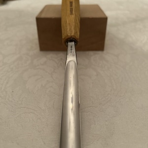 May include: A wood carving chisel with a wooden handle and a silver blade. The handle is light brown and has the text "SWISS MADE" printed on it. The blade is silver and has the number "7" etched on it.