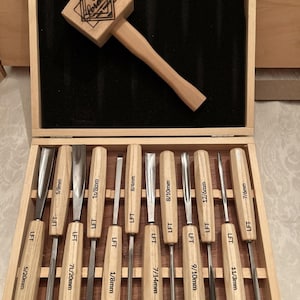 May include: A wooden mallet with a branded logo and a set of ten wood carving chisels with light wood handles and metal blades, all organized in a wooden storage box with black foam lining. Each chisel handle is marked with LFT and size labels.