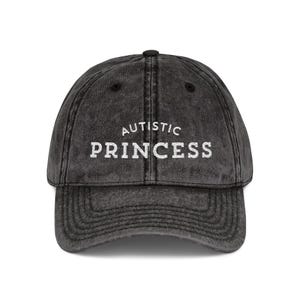 May include: A distressed black baseball cap with the words "AUTISTIC PRINCESS" embroidered in white block letters. The cap has a curved brim and an adjustable strap.