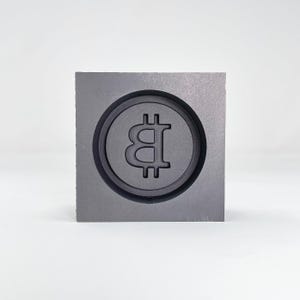 May include: A gray square mold with a circular indentation featuring a raised Bitcoin symbol.