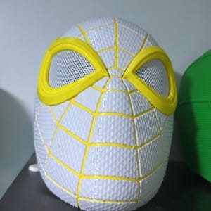 Puede incluir: Una m&aacute;scara de Spider-Man blanca y amarilla. La m&aacute;scara presenta una superficie texturizada con l&iacute;neas de telara&ntilde;a amarillas y contornos de ojos amarillos. Las aberturas para los ojos son de material de malla. Es un art&iacute;culo de cosplay o disfraz.