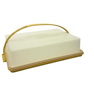 Puede incluir: Un recipiente rectangular para alimentos con tapa de color blanco roto y base dorada. El contenedor cuenta con un asa arqueada a juego de color dorado que está unida a los lados de la base, lo que permite transportar la unidad con facilidad.