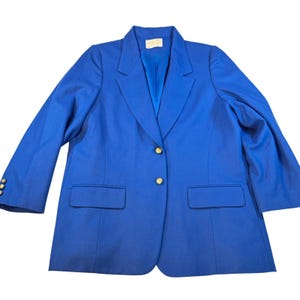 May include: A vibrant royal blue blazer with gold buttons. The jacket features a classic design with a notched collar, two front pockets, and three buttons on each cuff. The blazer is made of a smooth fabric.