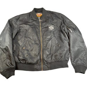May include: Black bomber jacket with a zip-up front, ribbed cuffs, and a collar. The jacket features a Harley-Davidson logo on the chest and a small pocket on the left sleeve. The jacket is made of a shiny material.