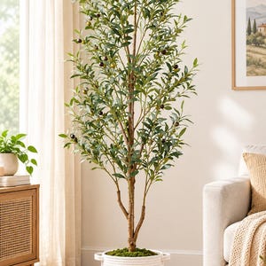 May include: A tall artificial olive tree with green leaves and small dark olives, featuring a textured brown trunk. The tree is planted in a two-toned cylindrical basket with a white rope top section and a tan woven rope base.